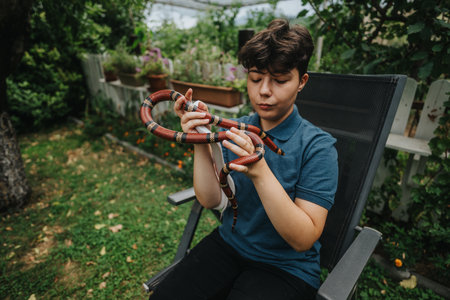 Young person calmly handling a colorful snake in garden settingの写真素材