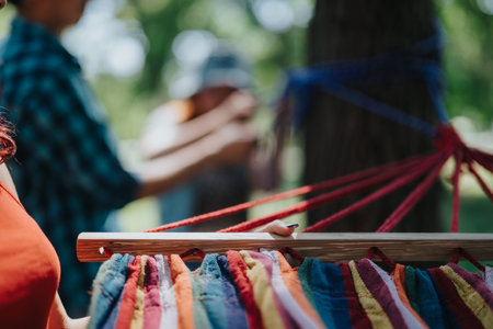 Friends setting up a colorful hammock in a park on a sunny dayの写真素材