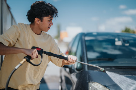 Young man washing car with pressure washer at self-service stationの写真素材