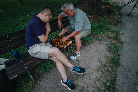 Two men playing chess in a park on a wooden bench