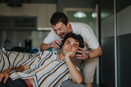 Young man playfully bothering friend listening to music on headphonesの写真素材