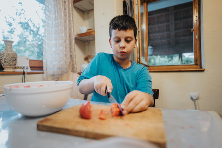 Young boy focused on chopping tomatoes in the kitchen