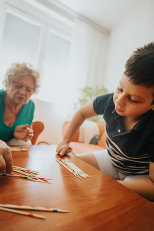 Young boy playing pick-up sticks with grandmother in cozy living roomの写真素材
