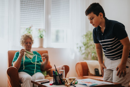 Grandmother knitting while nephew enjoys his meal in cozy living roomの写真素材