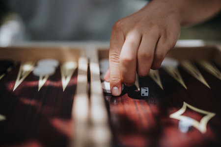 Close-up of hand rolling dice on a wooden backgammon board in a strategic and engaging game setting outdoors. Concept of leisure, concentration, and strategy.の写真素材