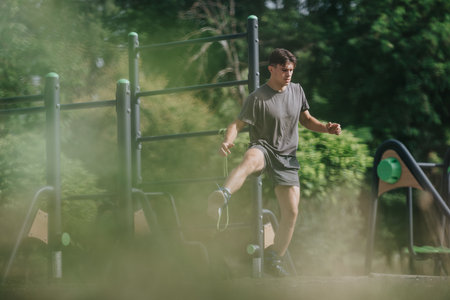 Young man performing outdoor workout in park using calisthenics equipment for fitness and strength...