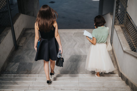 Women walking down stairs in urban setting carrying documents and bagsの写真素材