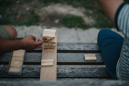 Close-up of hands playing wooden block stacking game outdoorsの写真素材