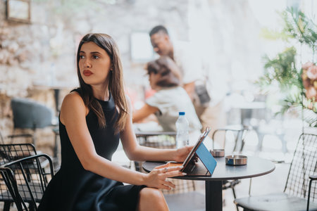 Woman using tablet in outdoor cafe, thoughtful and focused in casual environmentの写真素材