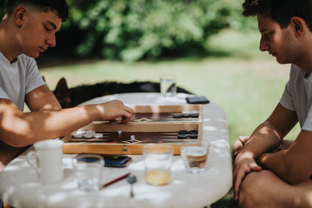 Two friends playing backgammon outdoors in a relaxed garden settingの写真素材