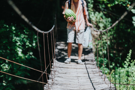 Man carrying watermelon on rustic wooden bridge in lush greeneryの写真素材