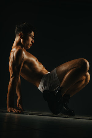 Athletic man performing intense body weight exercise on dark background showcasing strength and balanceの写真素材