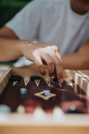 Close-up of a hand moving pieces in an intense backgammon game outdoors, capturing focus and strategy on a sunny day.の写真素材