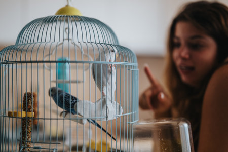 Young woman interacting with pet birds in a cage at home