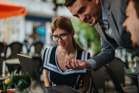 Business meeting with diverse professionals collaborating on a project with a laptop outdoors at a modern cafeの写真素材