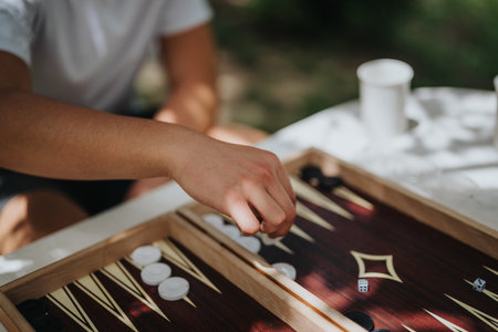 Close-up of hand playing backgammon outdoors on a sunny day with wooden board and dice in focus, evoking leisure and strategic thinkingの写真素材