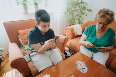 Grandmother and grandson playing cards together in a cozy living roomの写真素材