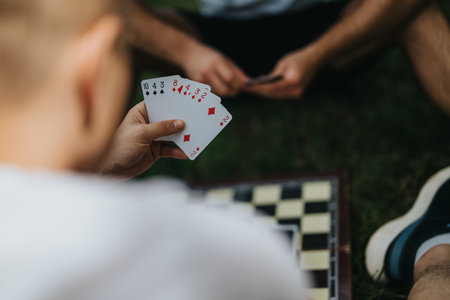 Friends playing card game and chess in a park settingの写真素材