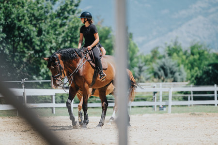 Young woman riding horse in outdoor arena surrounded by nature and mountainsの写真素材