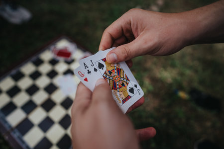 Hand holding playing cards over a chessboard during outdoor gameの写真素材