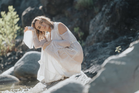 Woman in white dress posing outdoors near rocks and waterの写真素材