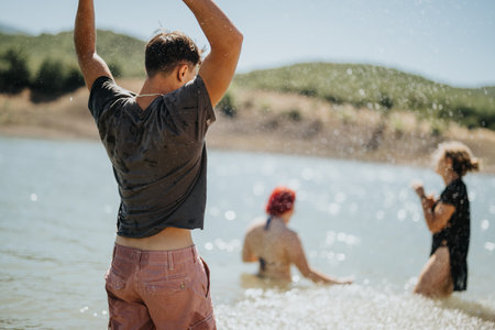 Friends having fun by a lake on a sunny day, splashing water and enjoying outdoor activitiesの写真素材
