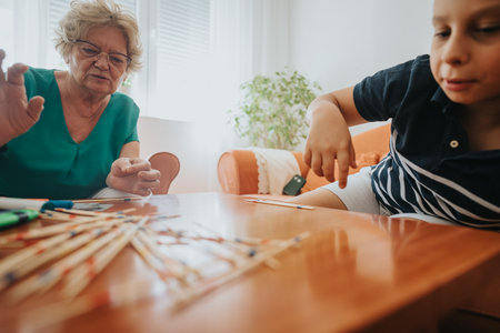 Young boy playing pick-up sticks with grandmother in cozy living roomの写真素材