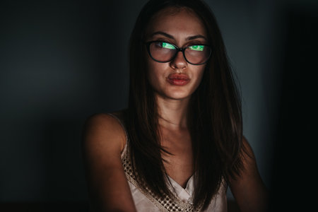 Focused woman with glasses working late at night in dim lightの写真素材