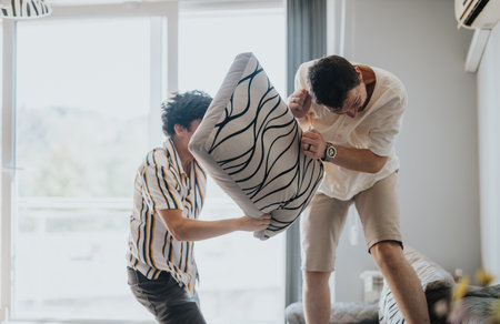 Friends having fun with a playful pillow fight indoorsの写真素材