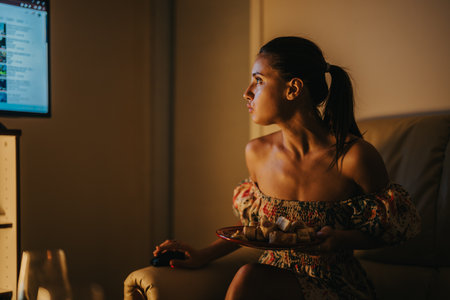 Woman watching late-night TV with snacks in cozy home settingの写真素材