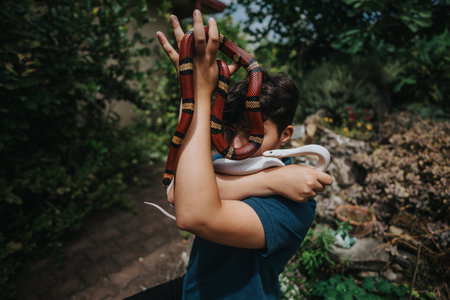 Young girl in a garden holding colorful snakes with curiosityの写真素材