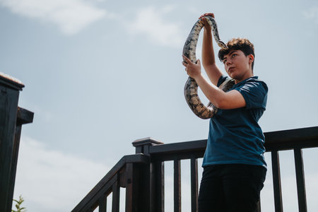Person confidently handling a large snake on a sunny day outdoorsの写真素材