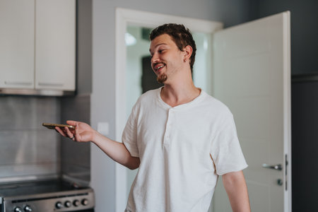 Man smiling while holding smart phone in modern kitchenの写真素材