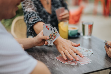 Friends enjoying a lively card game outdoors over drinksの写真素材
