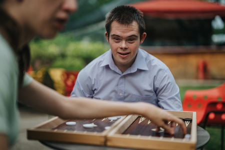 Boy with Down syndrome and girl in wheelchair playing backgammon outdoorsの写真素材