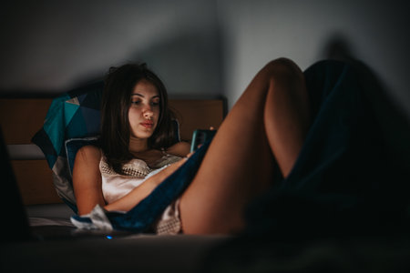 Young woman using smart phone while lounging in bed at night