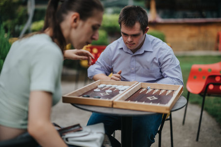 Boy with Down syndrome and girl in wheelchair playing backgammon outdoorsの写真素材