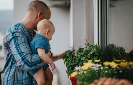 Father and baby exploring potted plants on a balcony togetherの写真素材