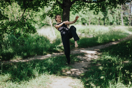 Young woman performing modern dance in a serene natural environment with lush green surroundingsの写真素材