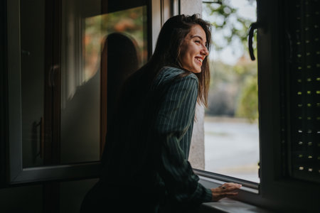 Joyful young woman smiling while leaning out of a windowの写真素材