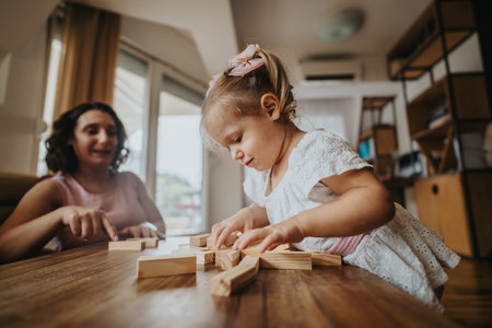 Mother and daughter playing with wooden blocks at home, enjoying quality time togetherの写真素材