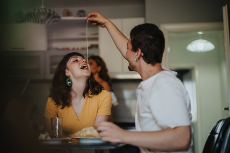 Couple enjoying playful pasta meal in cozy kitchen settingの写真素材