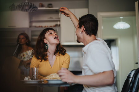 Friends enjoying a playful pasta meal at home togetherの写真素材