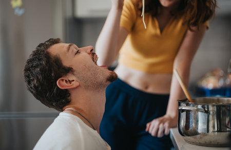 Couple enjoying playful cooking moment in cozy kitchenの写真素材