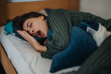 Woman yawning in bed under cozy striped bedding