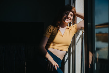 Smiling woman enjoying sunlight by the window in cozy roomの写真素材