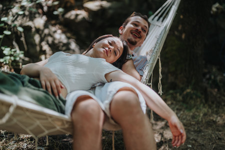 Couple relaxing on a hammock under trees in a serene outdoor settingの写真素材