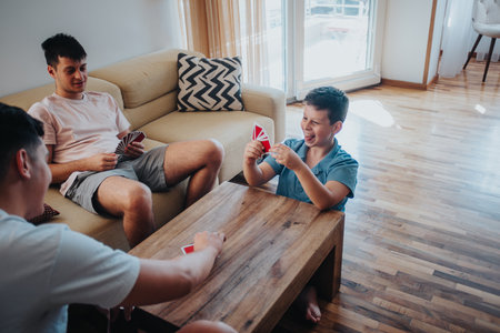 Older teenagers playing a card game with their younger brother in a cozy living roomの写真素材