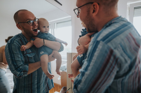 Father joyfully holding baby in front of mirror at homeの写真素材