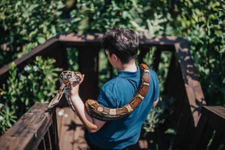 Young boy enjoying outdoor adventure with pet snake on wooden deckの写真素材